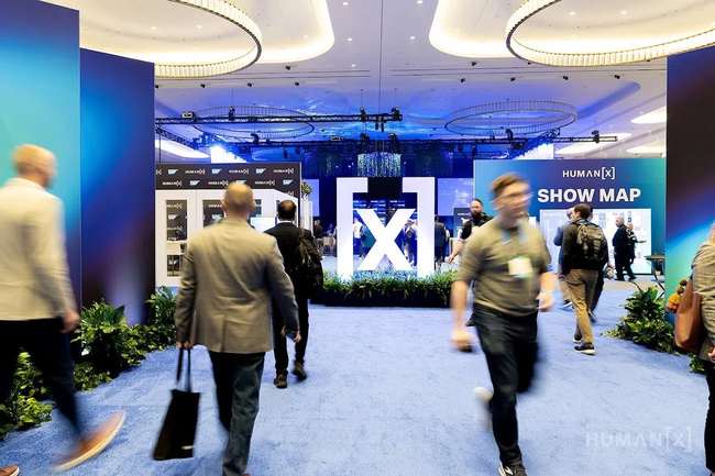 HumanX 2026 — main expo entrance with illuminated [x] sculpture, SHOW MAP wall, and conference attendees walking through the venue
